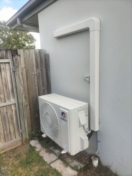 Gree outdoor unit beside a timber fence, pipework run up the wall in a neat cover
