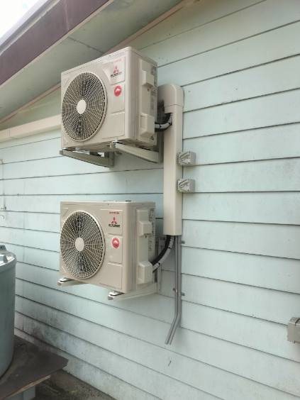 Two Mitsubishi Heavy Industries units stacked on wall brackets, pipes in one cover