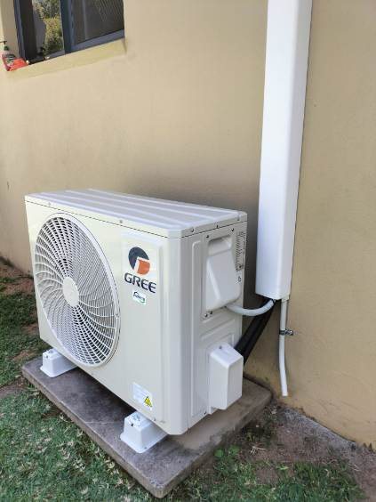 Gree outdoor unit on a pad against a rendered wall, pipe cover to the eaves